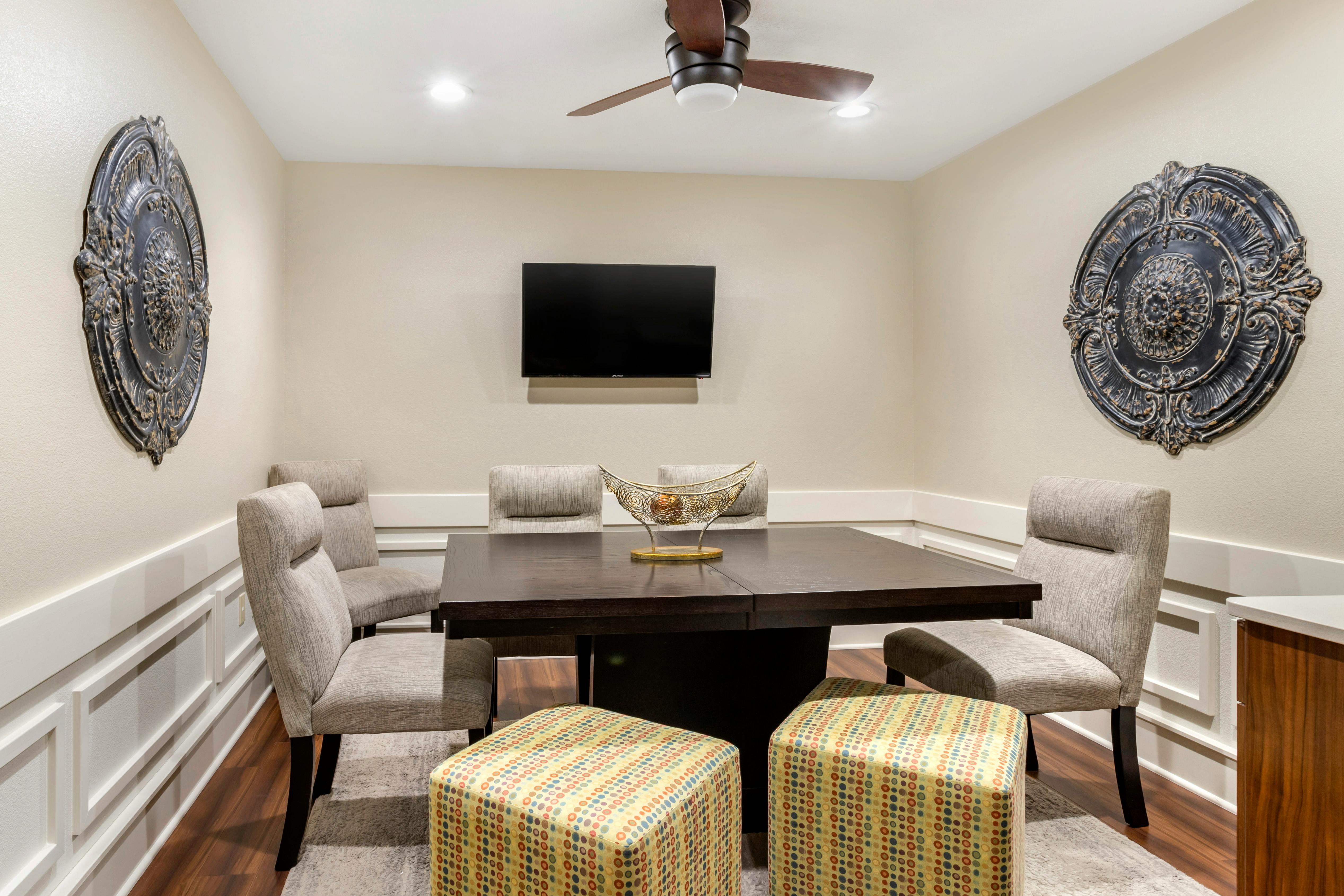 Dark dining table with gray chairs and two patterned ottomans