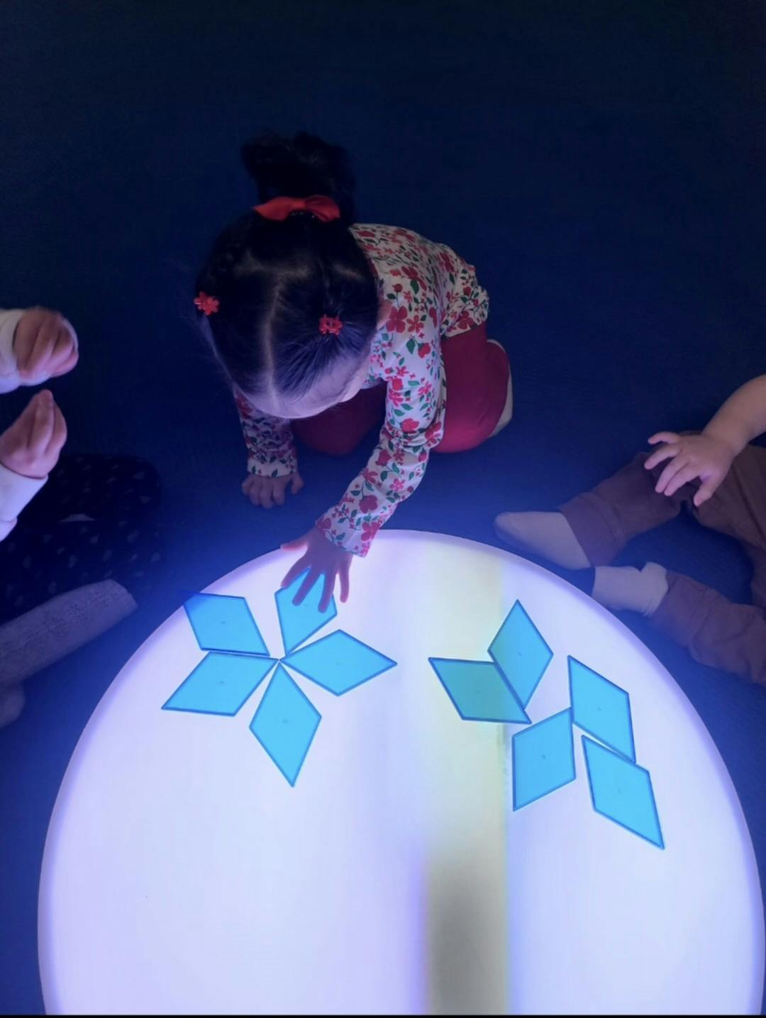 Child playing with light-up shapes on a glowing table