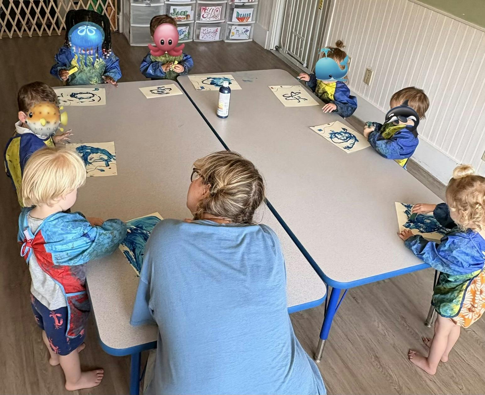 Group of children and an adult painting at a table in a classroom