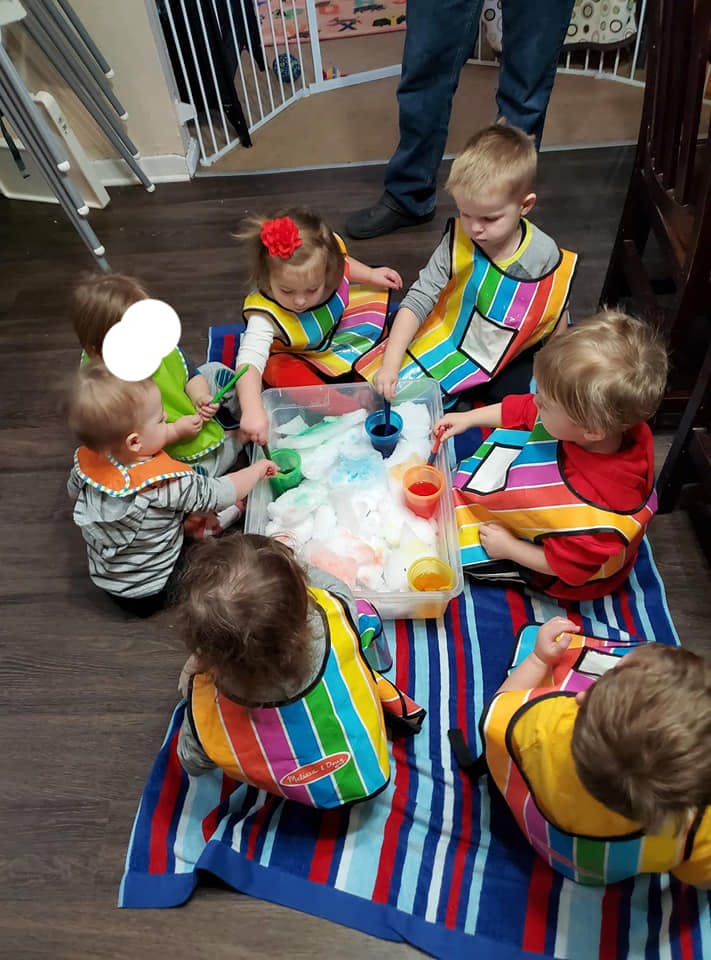Children in colorful smocks playing with a sensory bin