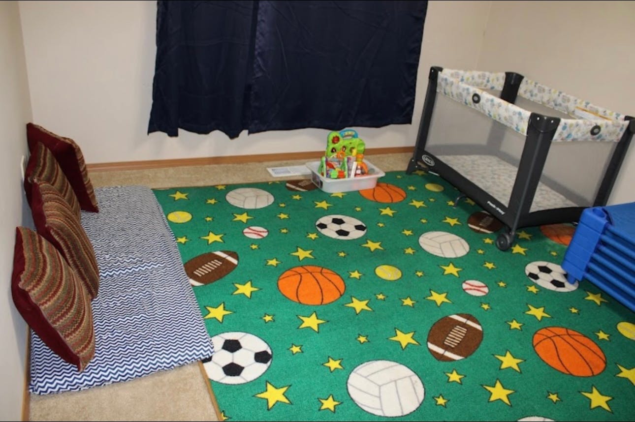 Playroom with a green sports-themed rug, cushions, and a playpen