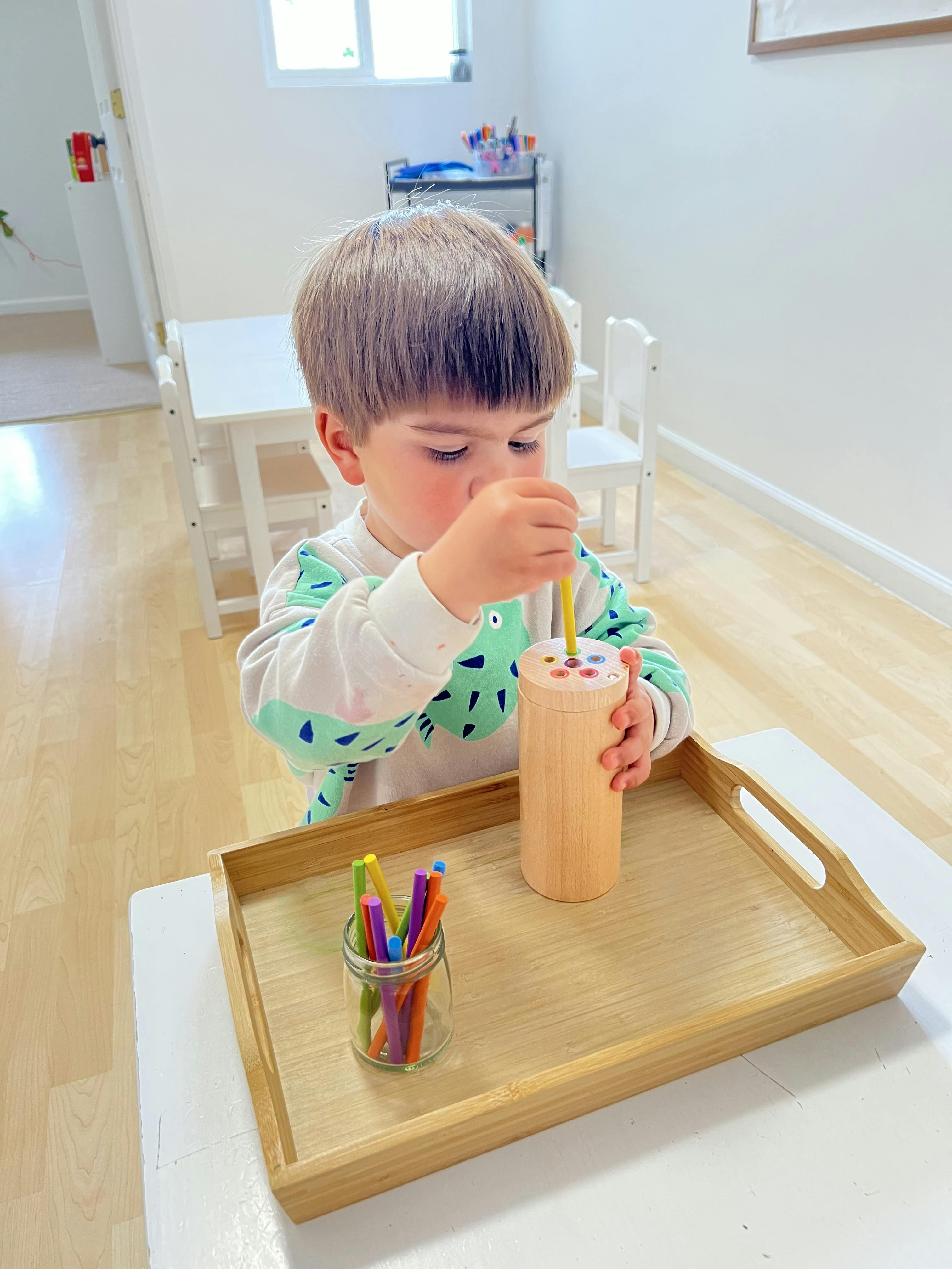 Child placing a yellow stick into a wooden sorting toy