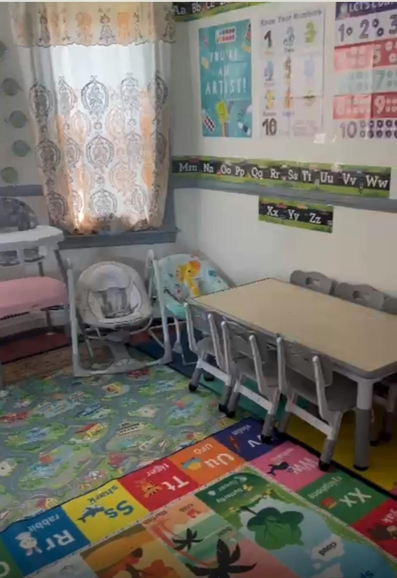 Classroom with small table and chairs, baby swings, and alphabet rug