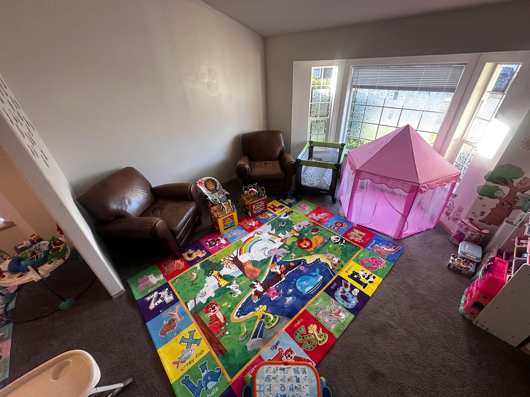Playroom with a colorful rug, two armchairs, and a pink play tent