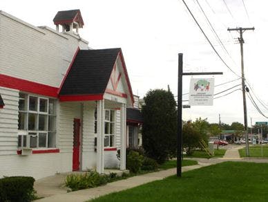 White building with red trim and black roof next to a sidewalk and street sign