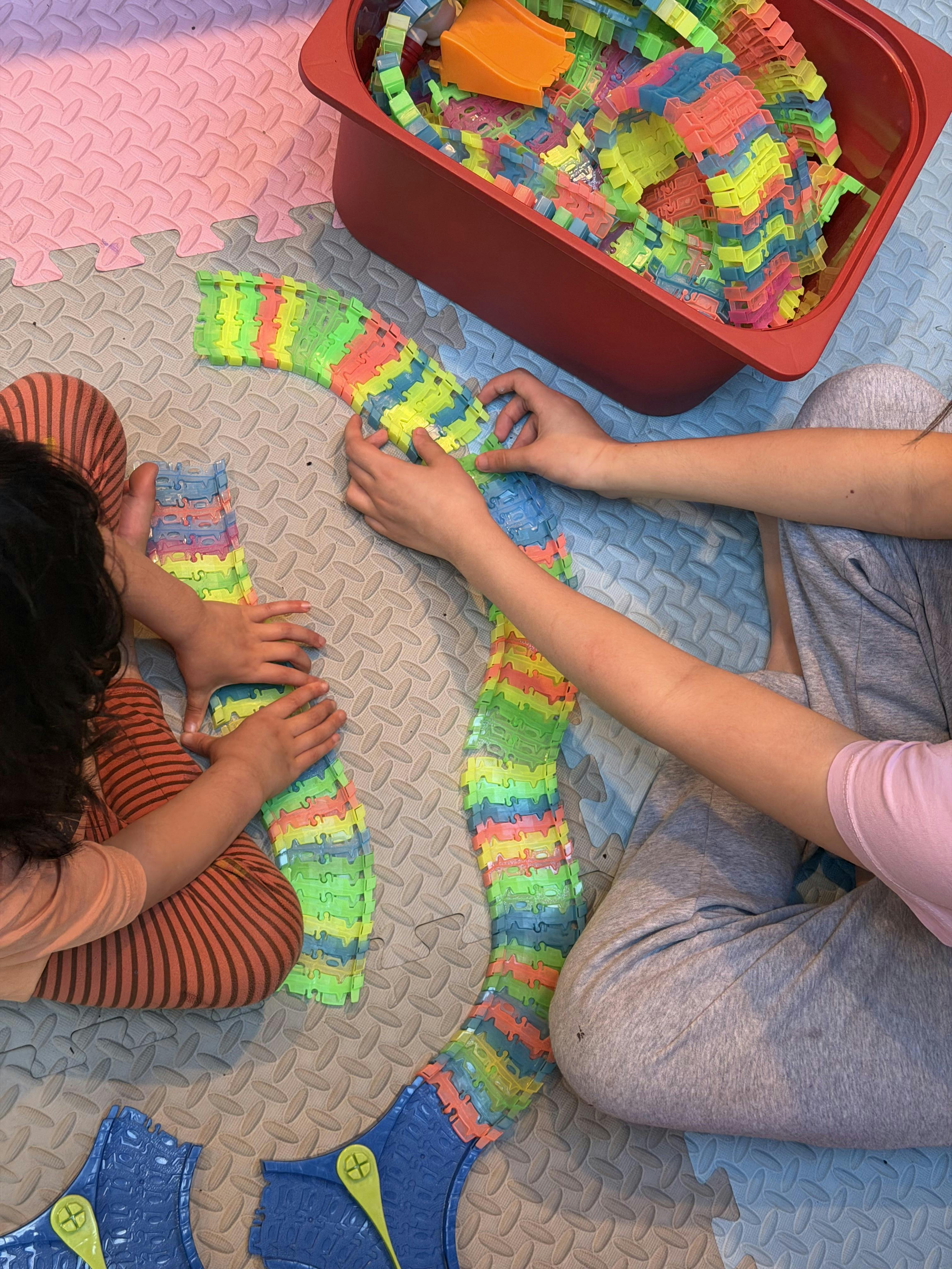 People connecting colorful plastic track pieces on a floor mat