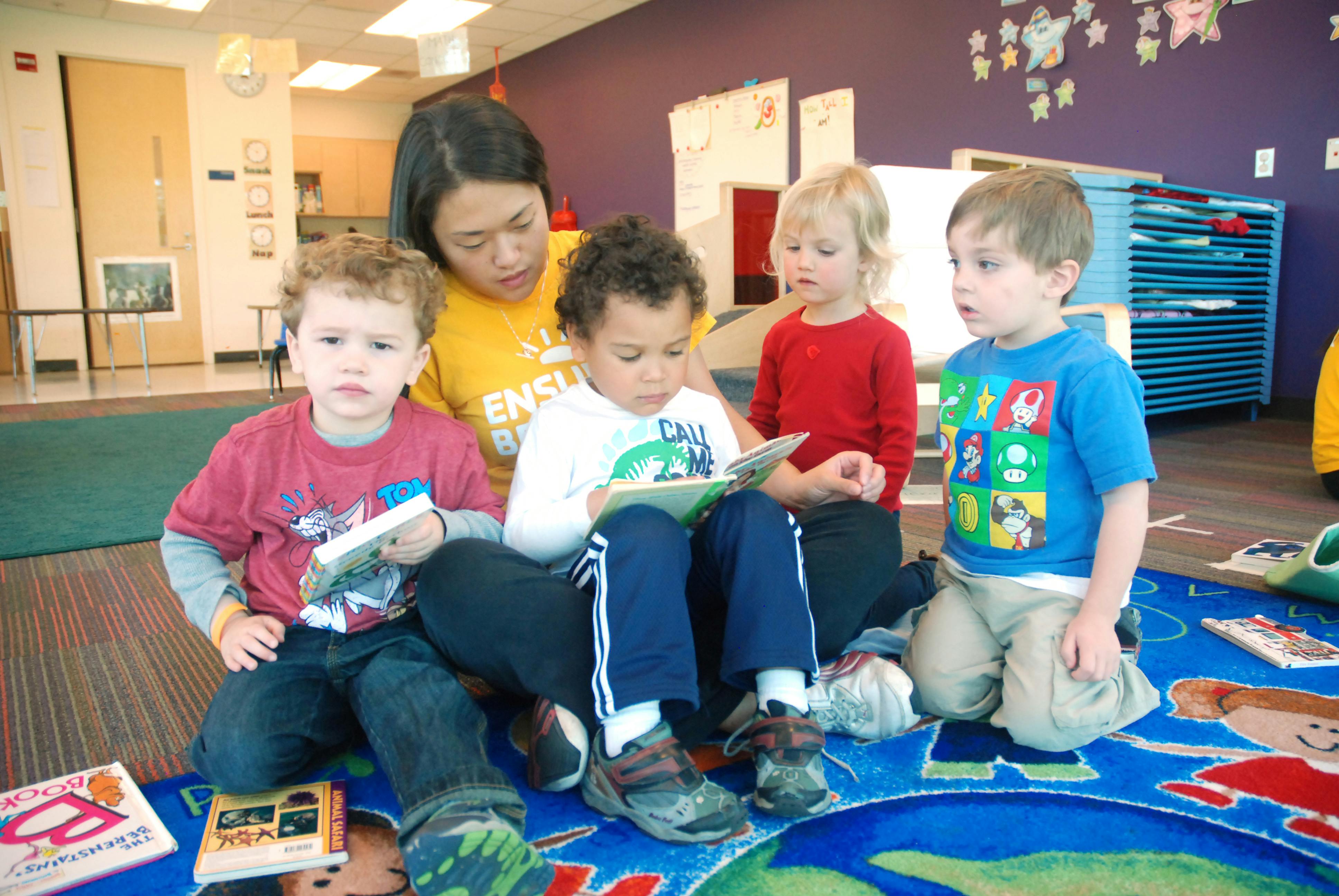 Adult person reading to three children sitting on a rug