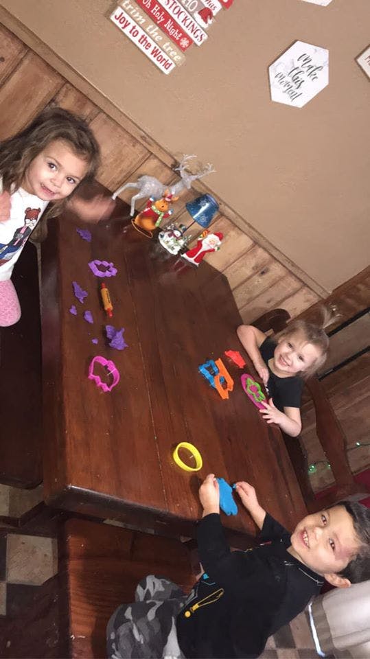Three children playing with colorful dough and cookie cutters on a table