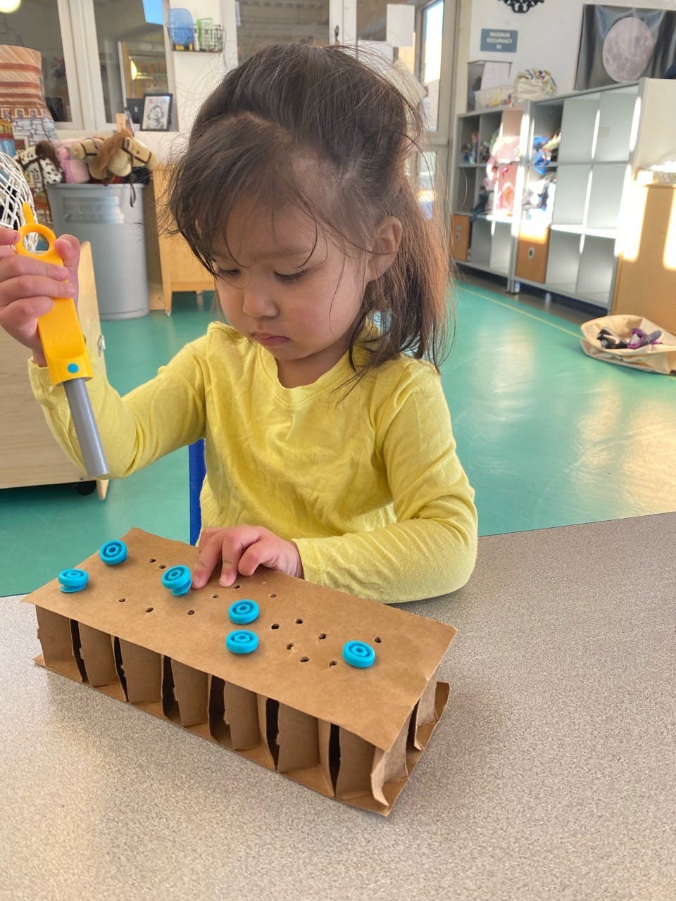 Child playing with a toy hammer and a cardboard box with blue pegs