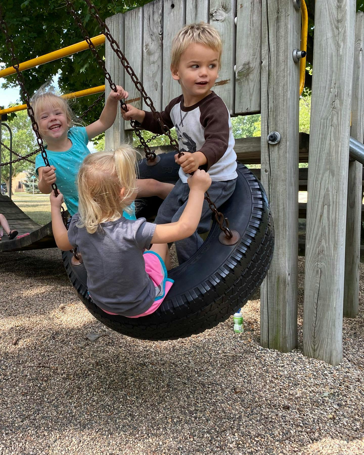 Three children playing on a tire swing at a playground