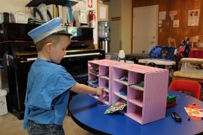 Child in a hat reaching into a pink cubby organizer on a blue table