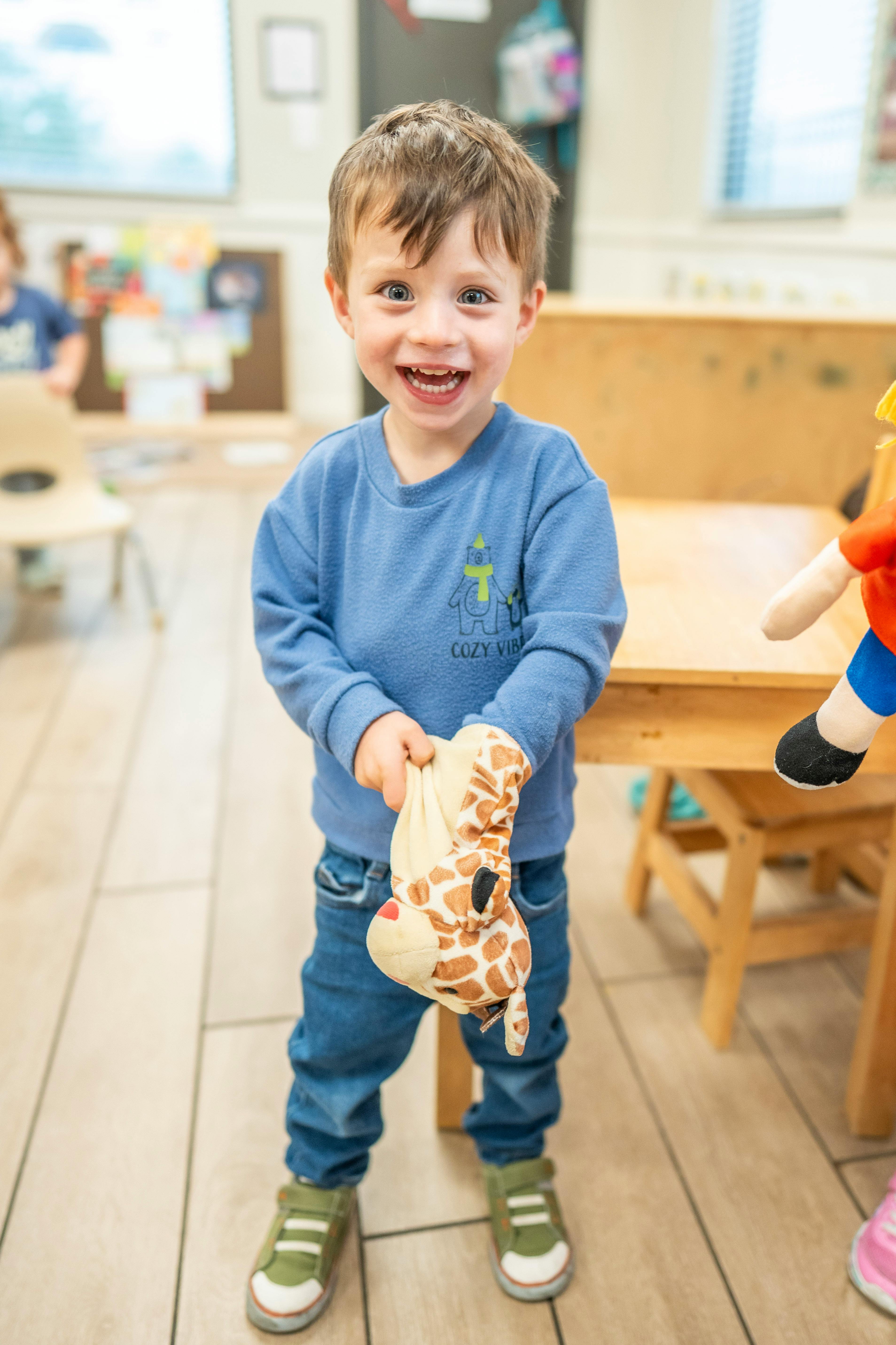 Child holding a giraffe plush toy in a classroom