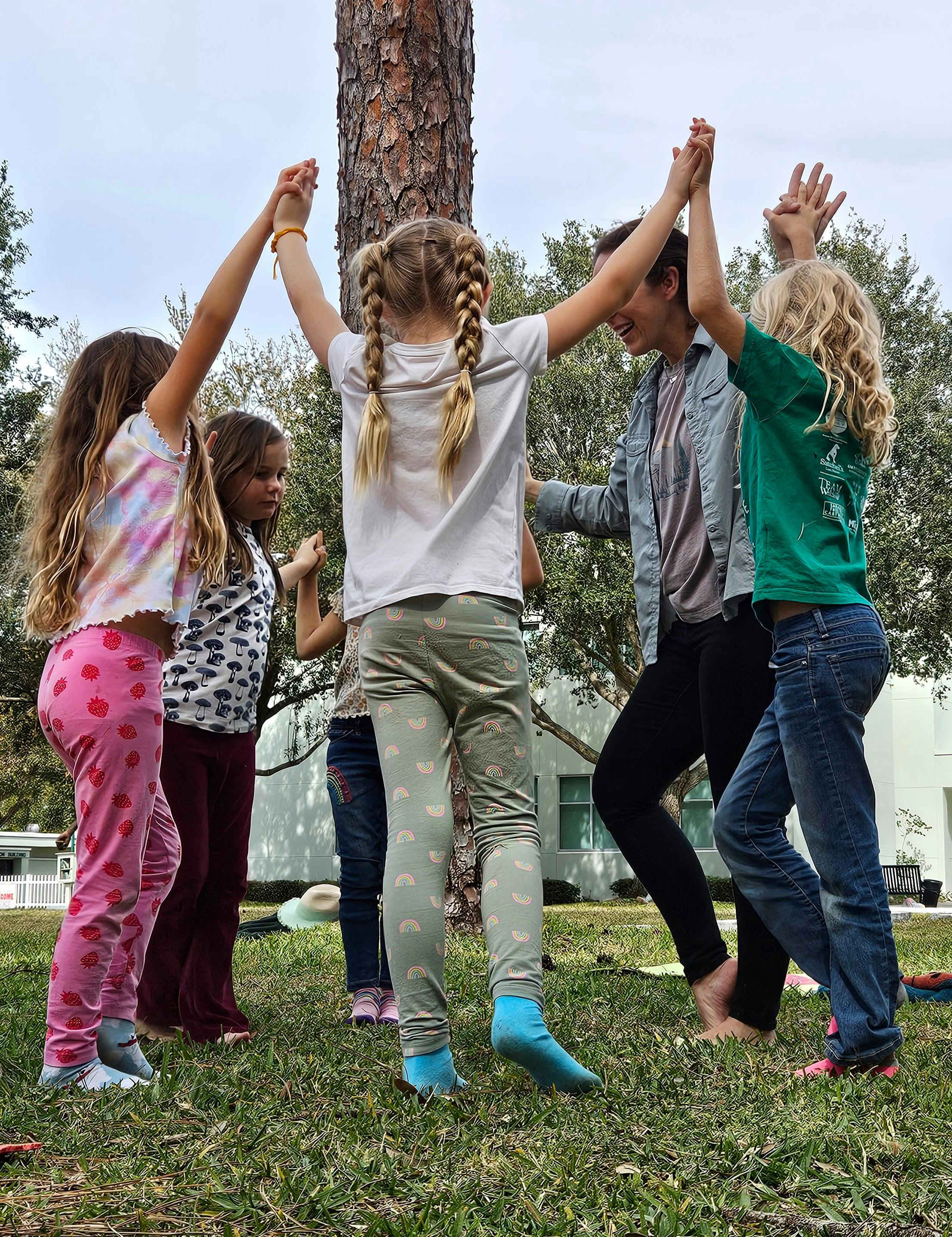 Children and an adult holding hands in a circle around a tree