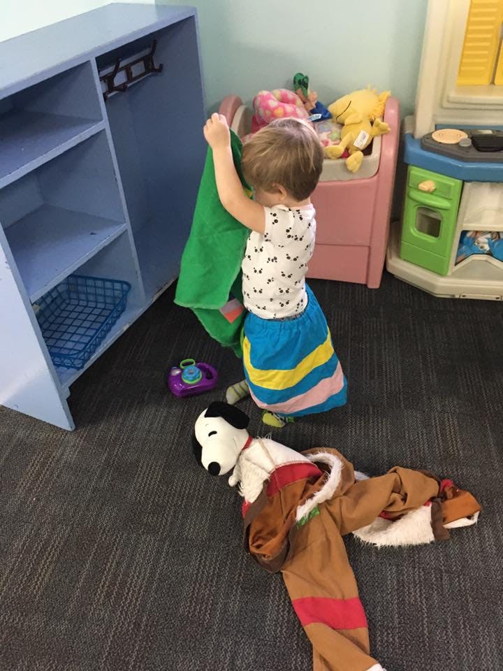 Child holding a green blanket next to a blue shelf