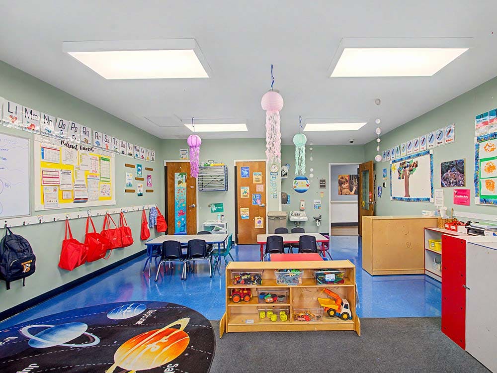 Colorful classroom with small tables and chairs, shelves with toys, and decorated walls