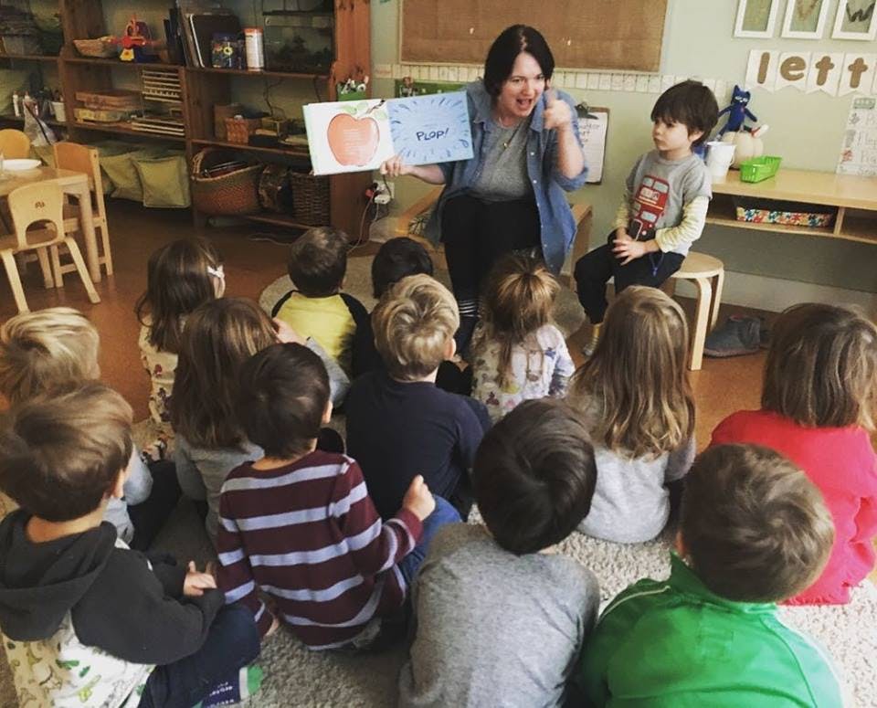 Person reading a book to a group of children in a classroom
