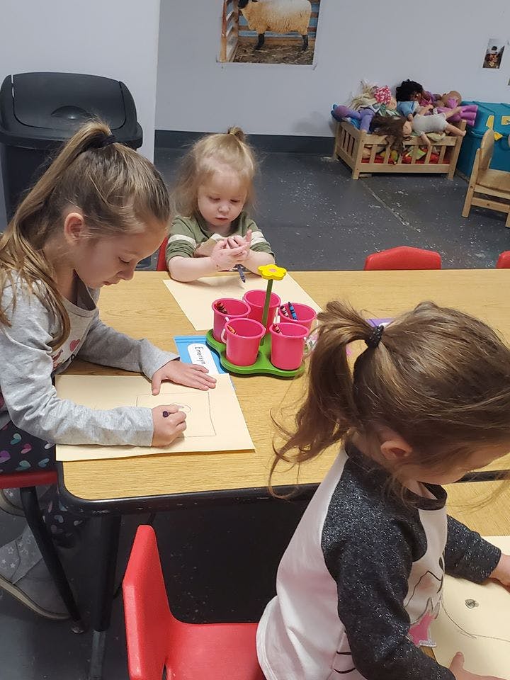 Three children drawing at a table in a classroom
