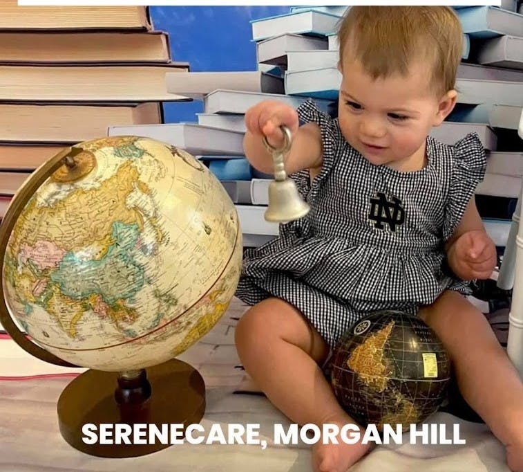 Child holding a bell next to a globe with books in the background