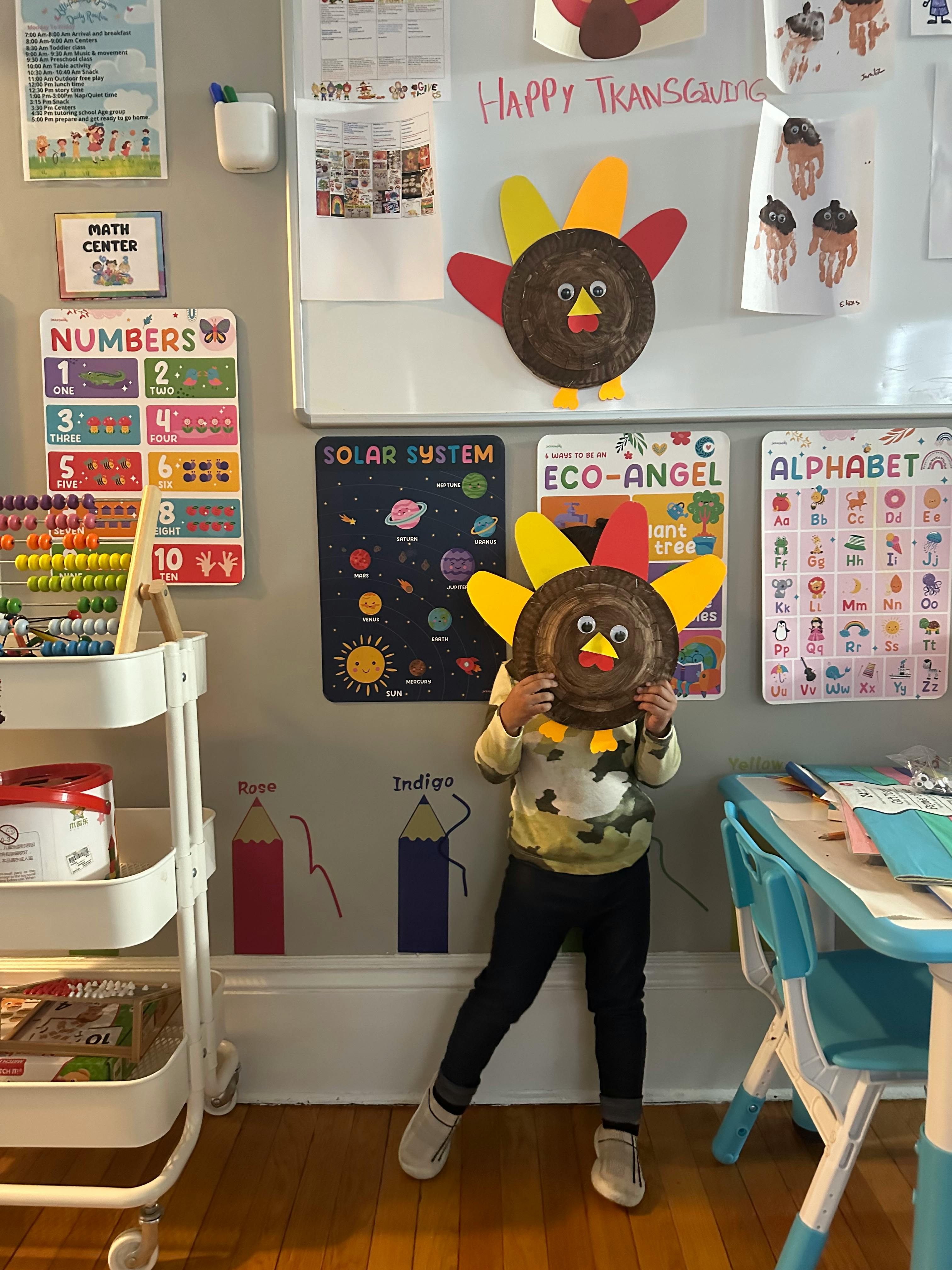 Child holding a turkey craft over their face in a classroom