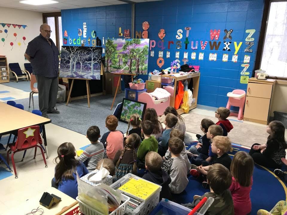 Adult presenting to a group of children seated on the floor in a classroom