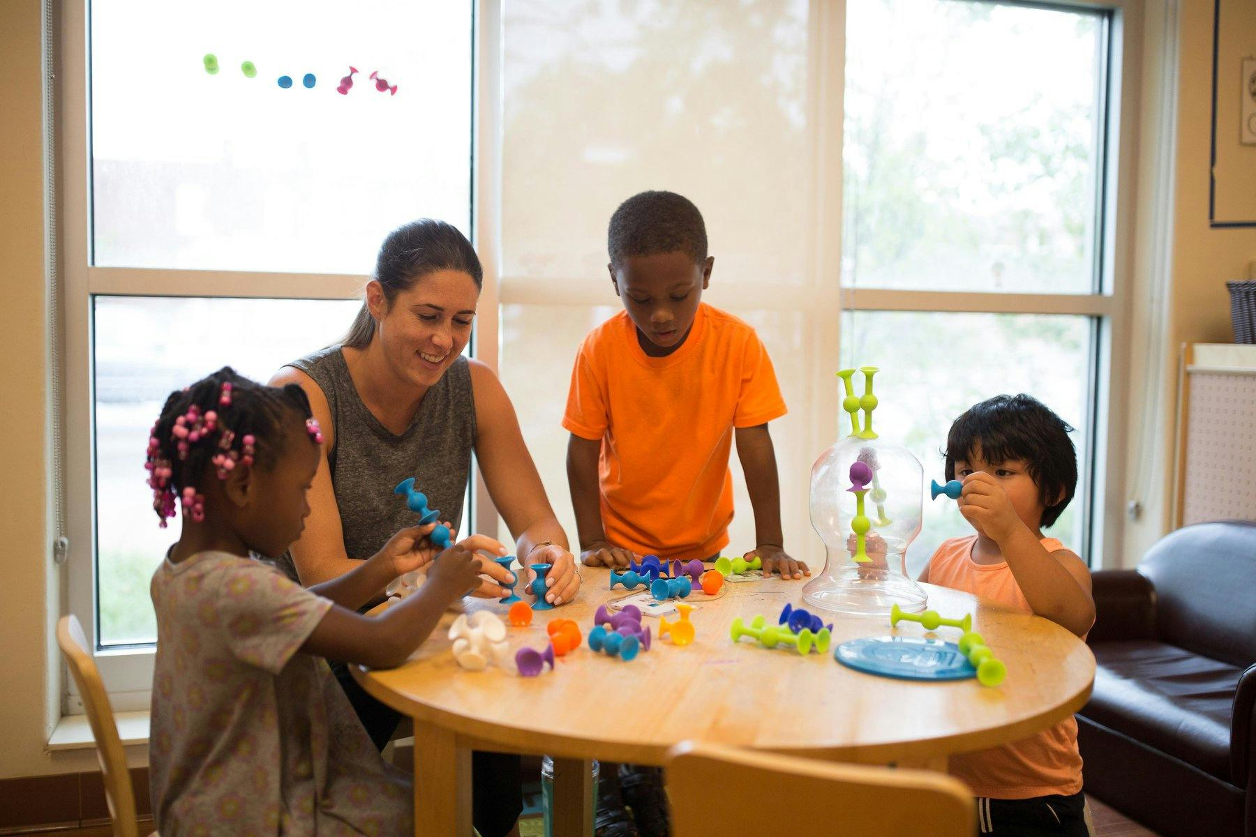 Adult and three children playing with toys at a table