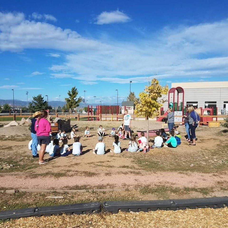 Adults and children sitting on the ground in a circle outdoors