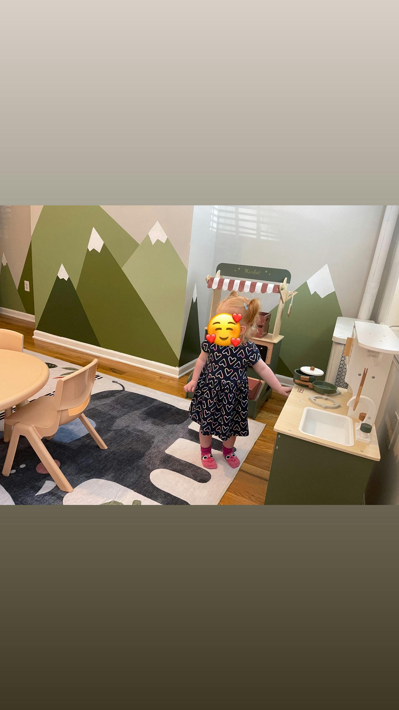 Child standing in a play area with a toy kitchen