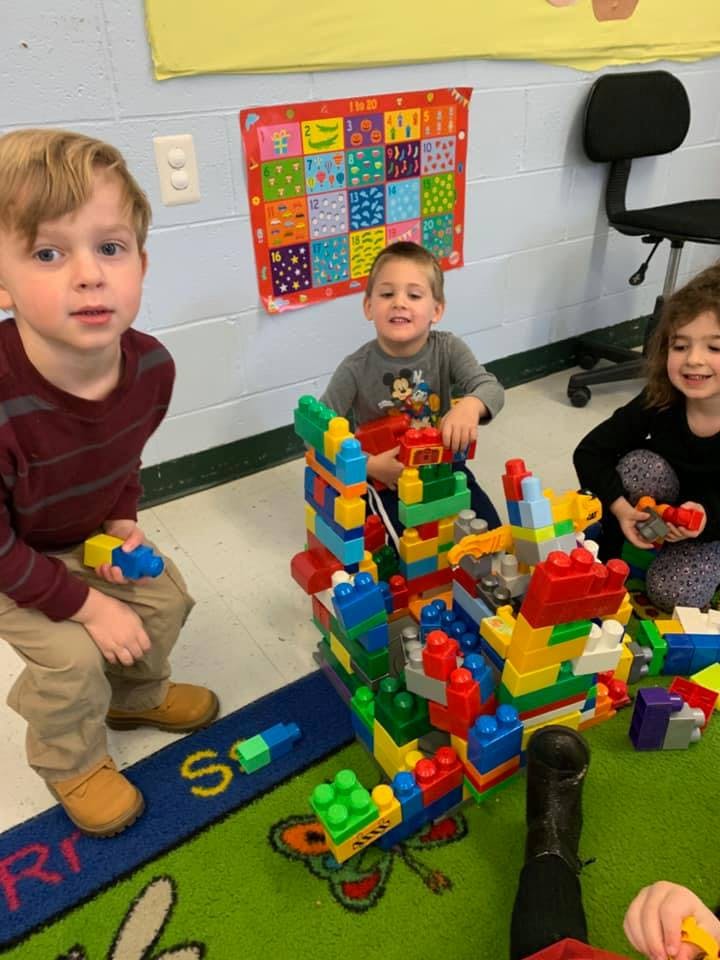 Three children playing with colorful building blocks in a classroom