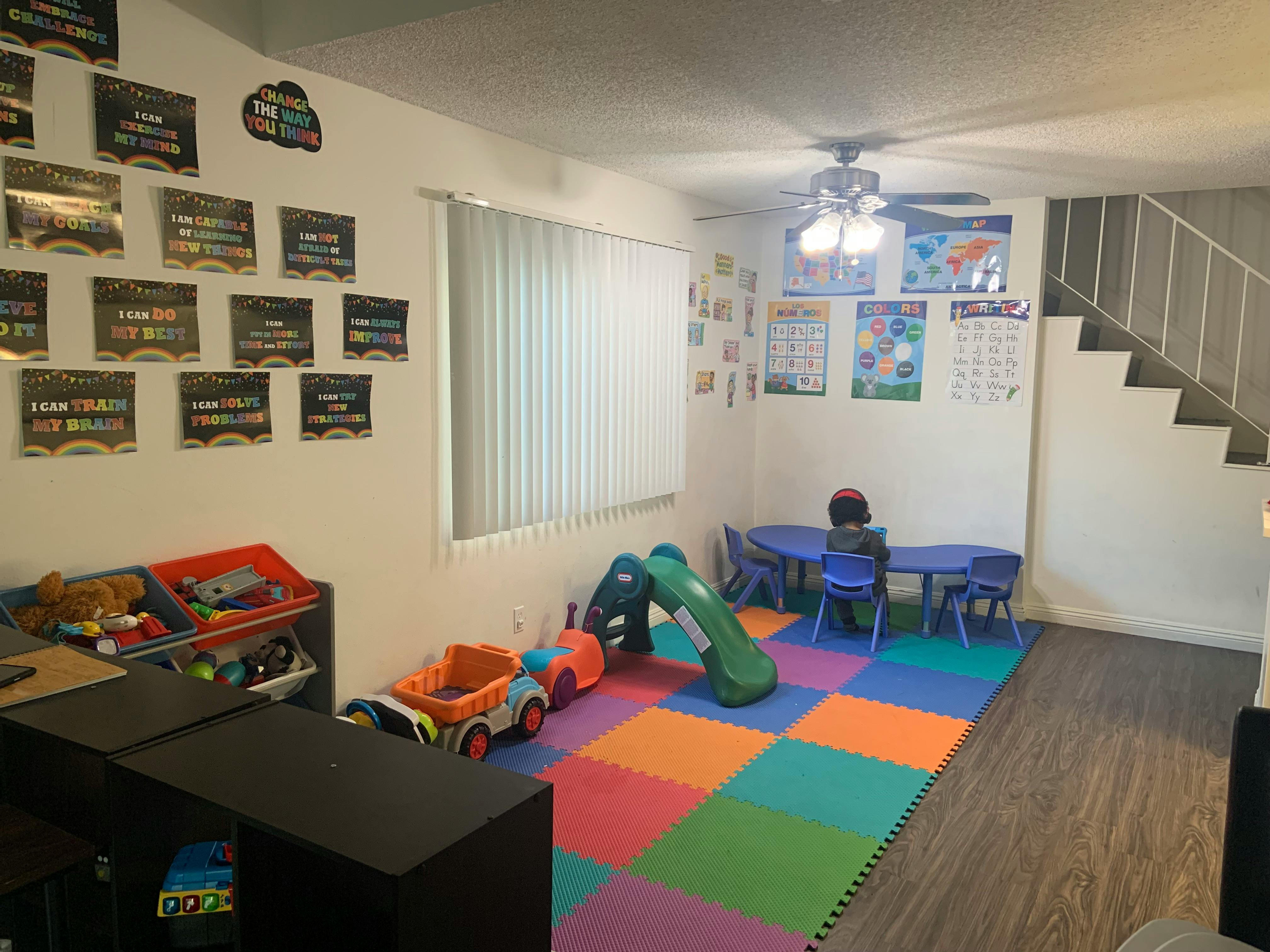 Child sitting at a small table in a playroom with colorful floor mats