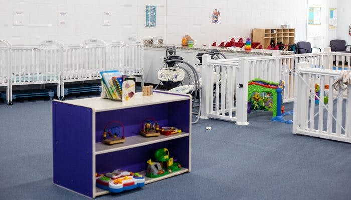 Nursery room with multiple white cribs and a purple toy shelf
