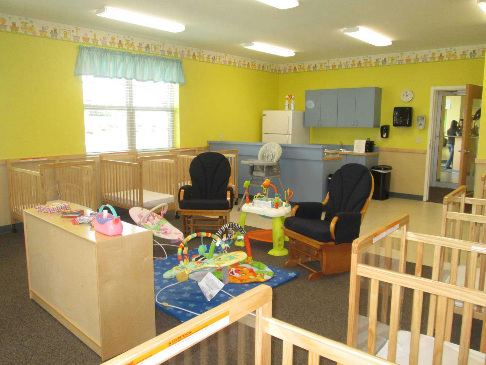 Nursery room with multiple cribs, rocking chairs, and baby play items