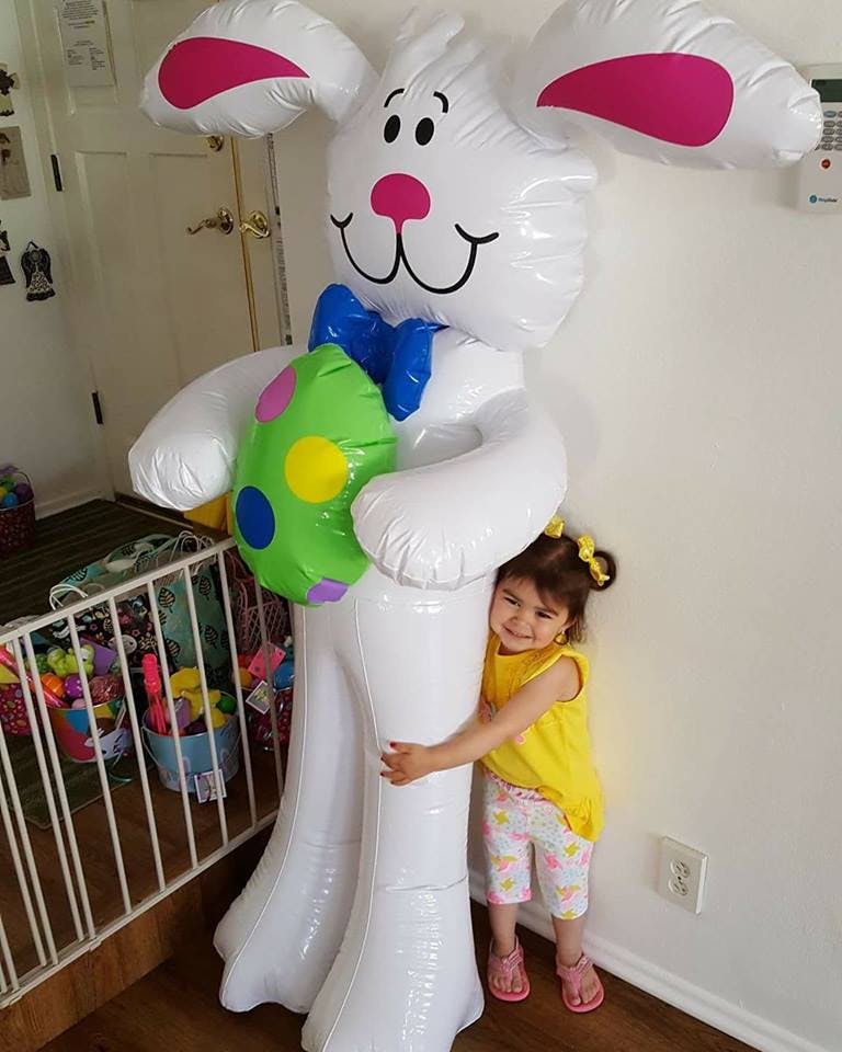 Child hugging a large inflatable white bunny holding a green egg