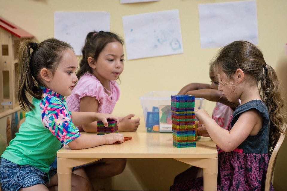 Three children playing with colorful blocks at a table in a classroom