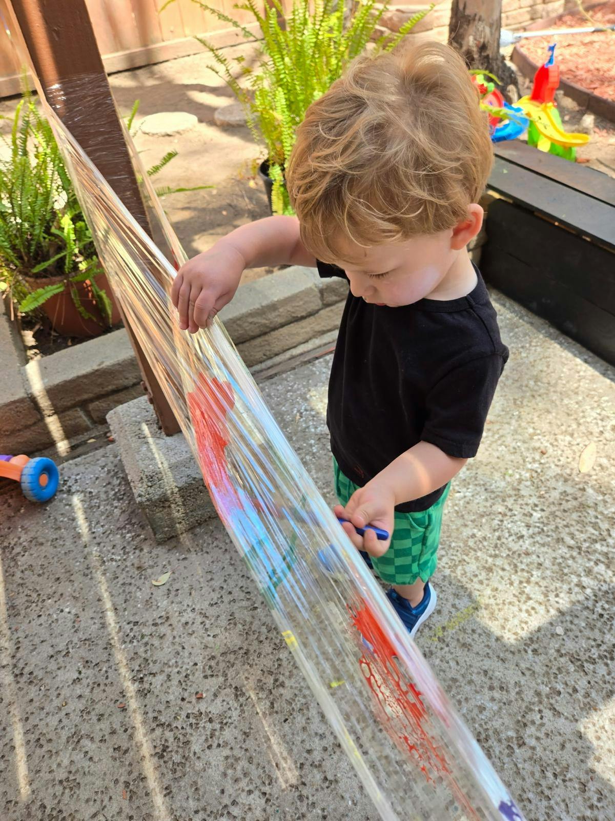 Child painting on plastic wrap stretched between poles outdoors