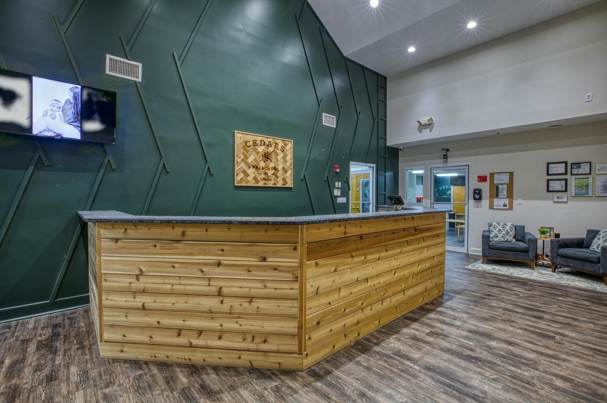 Reception desk with wood paneling, dark green wall, and a sign for Cedars Preschool