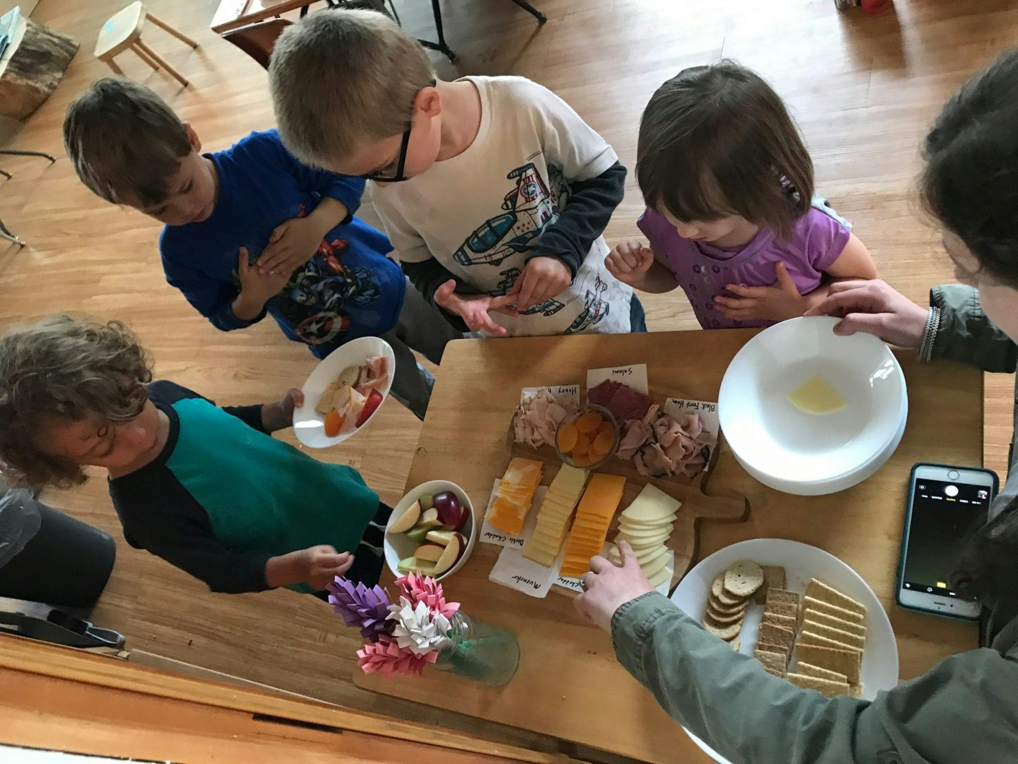 Children and adults gathered around a table with a cheese and cracker board