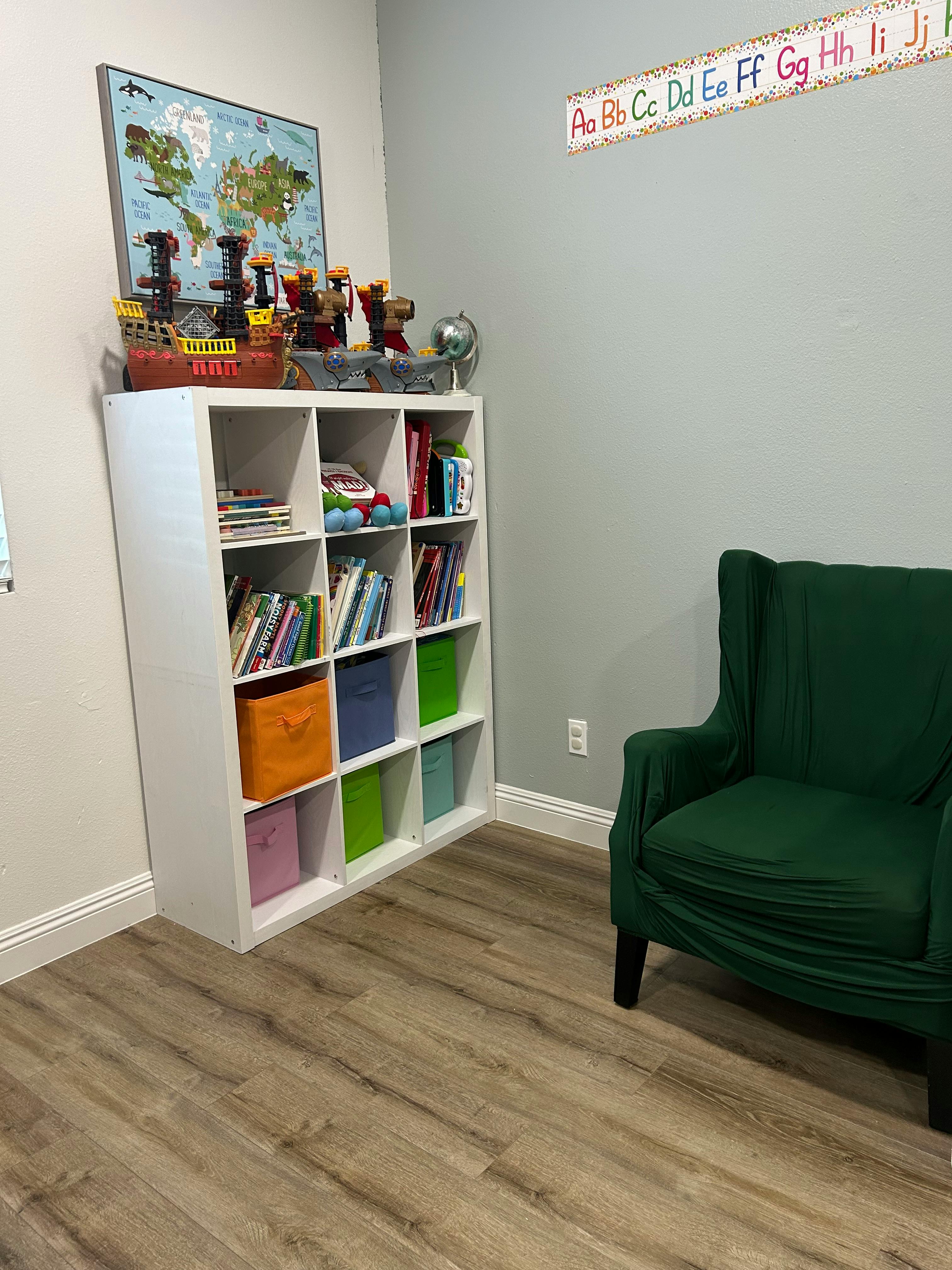 Bookshelf with books and storage bins next to a green armchair