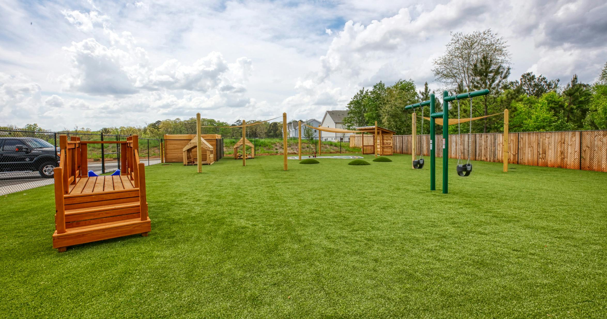 Outdoor playground with swings, wooden play structures, and artificial grass