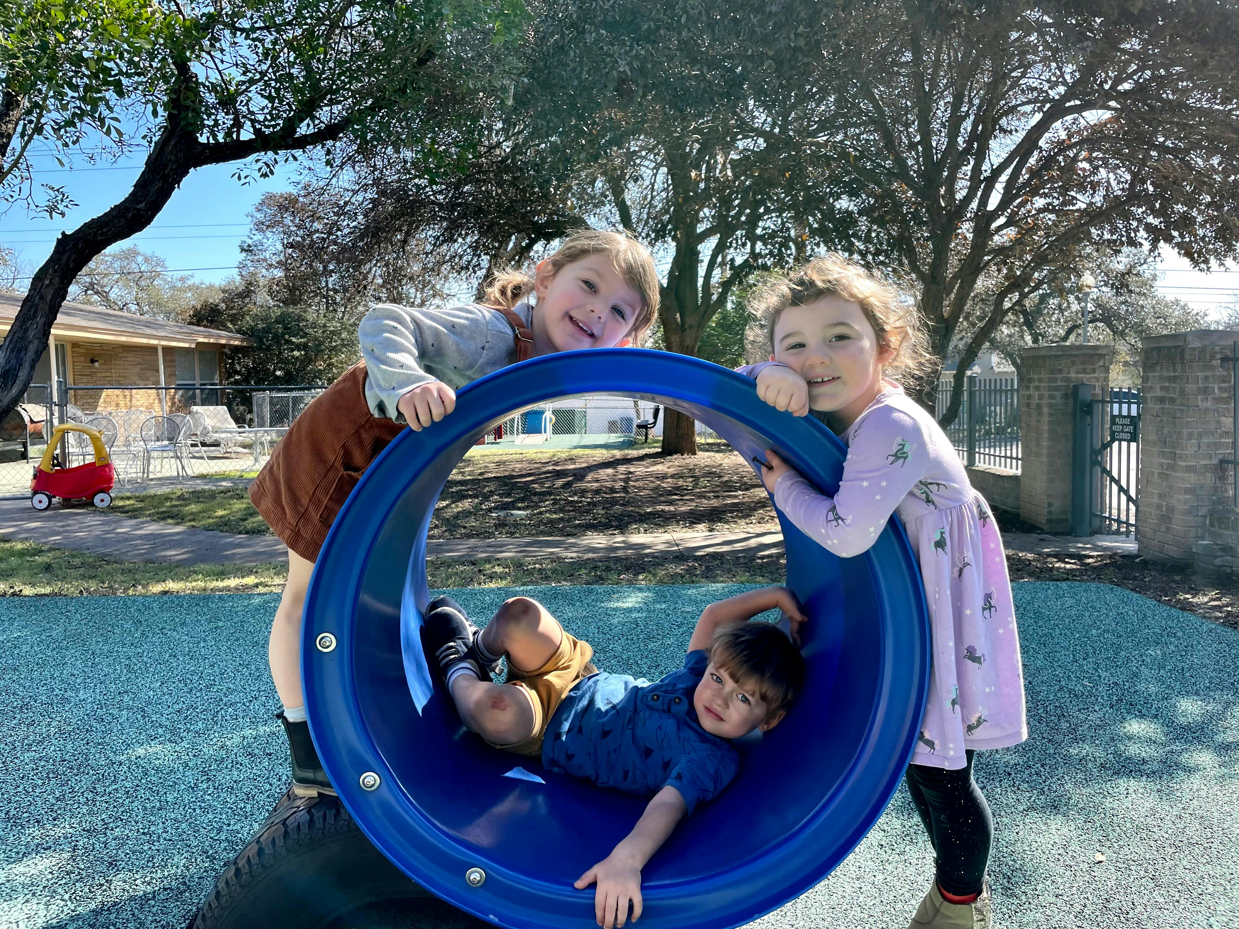 Three children playing on a blue tunnel slide