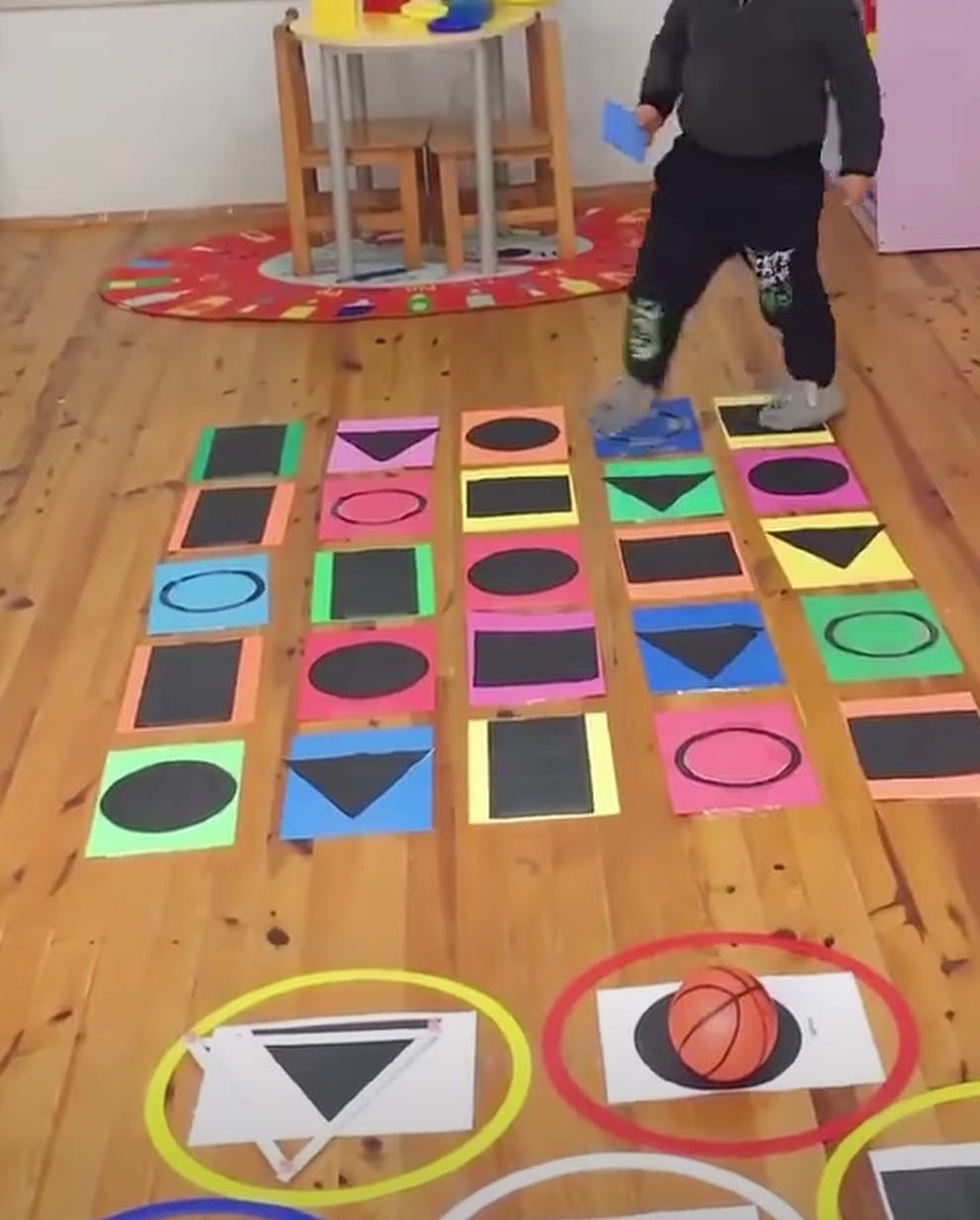 Child stepping on colorful shape cards on a wooden floor