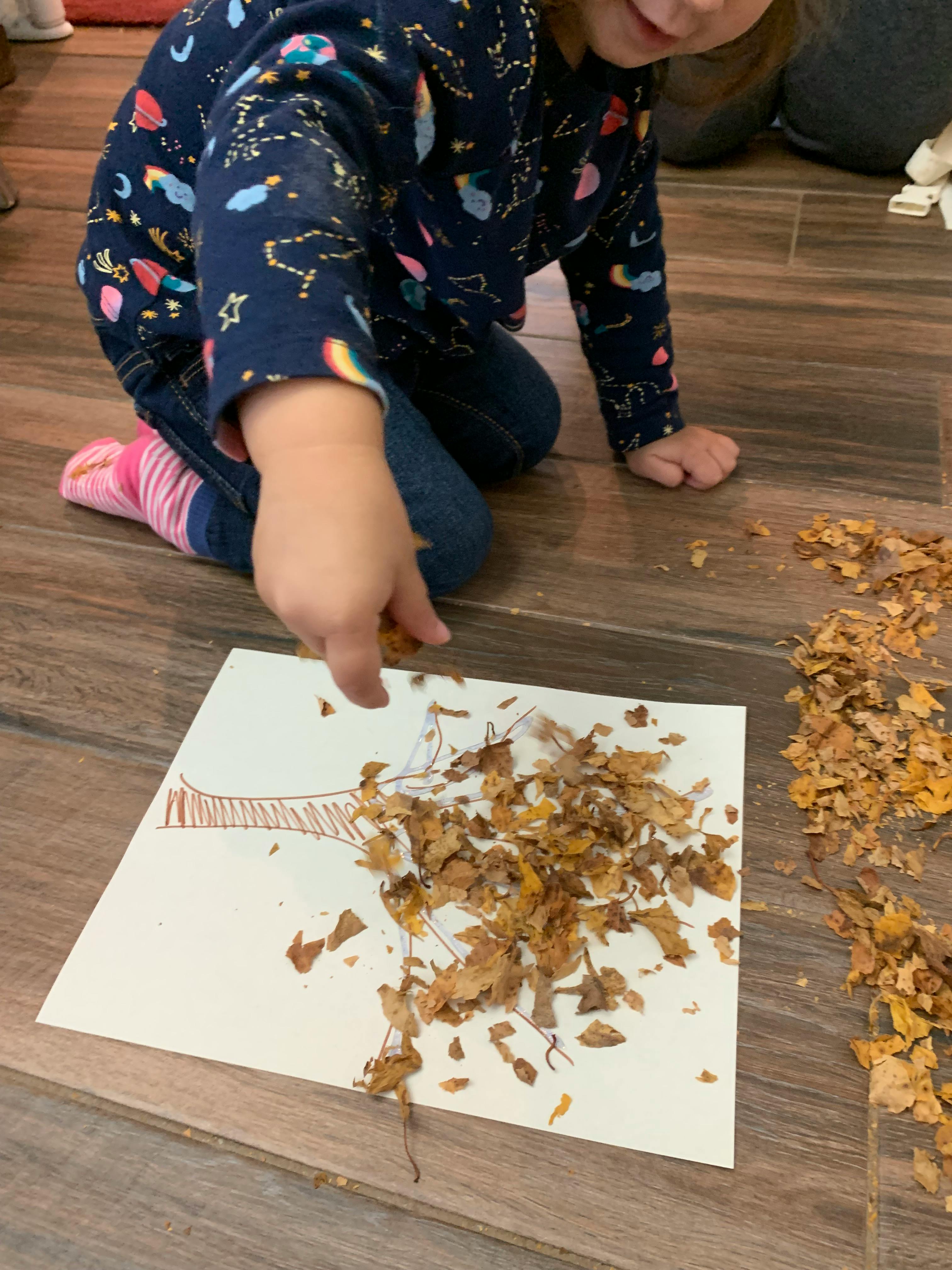 Child gluing leaves onto a drawing of a tree
