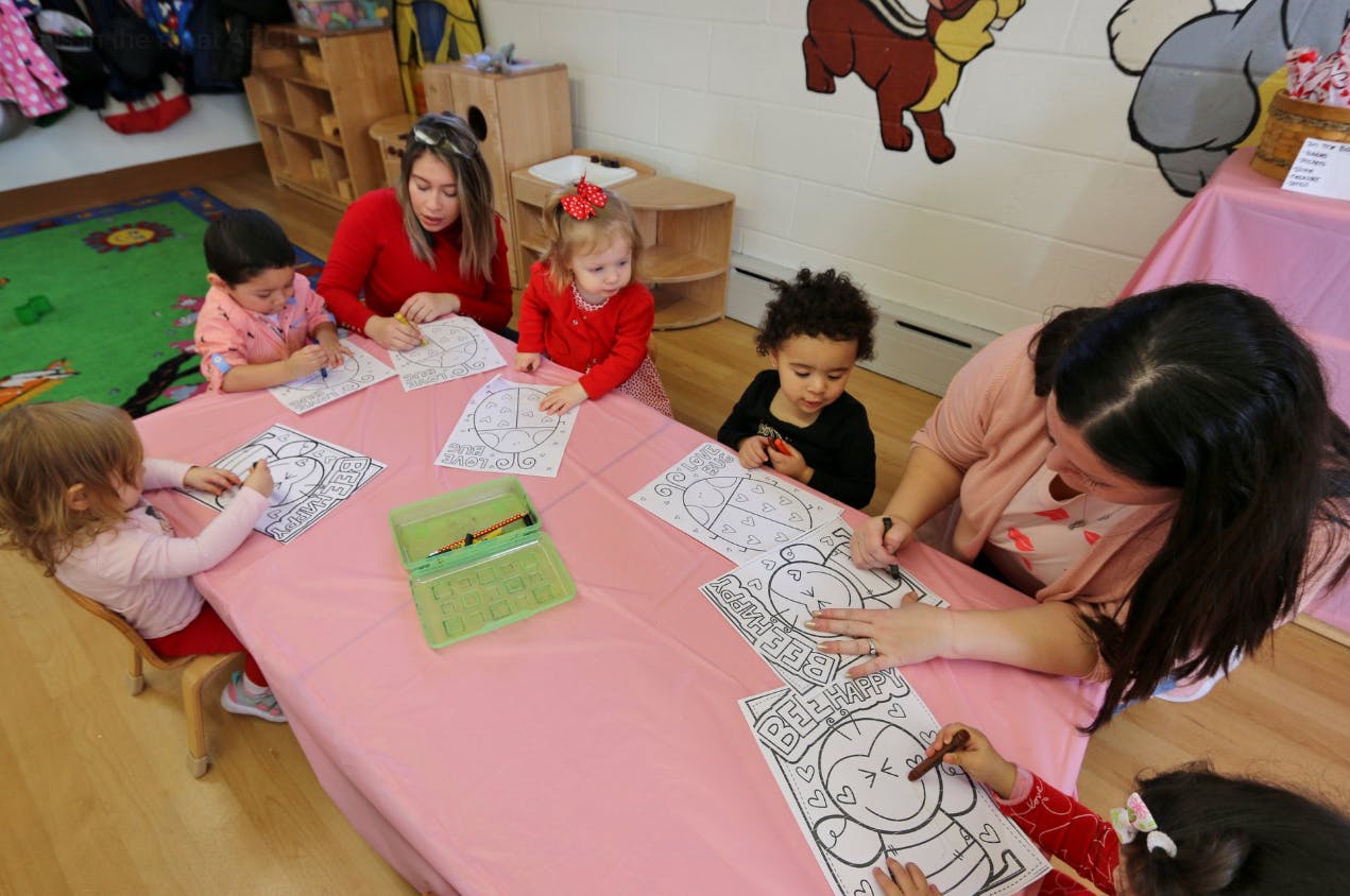 Adults and children coloring at a table in a classroom
