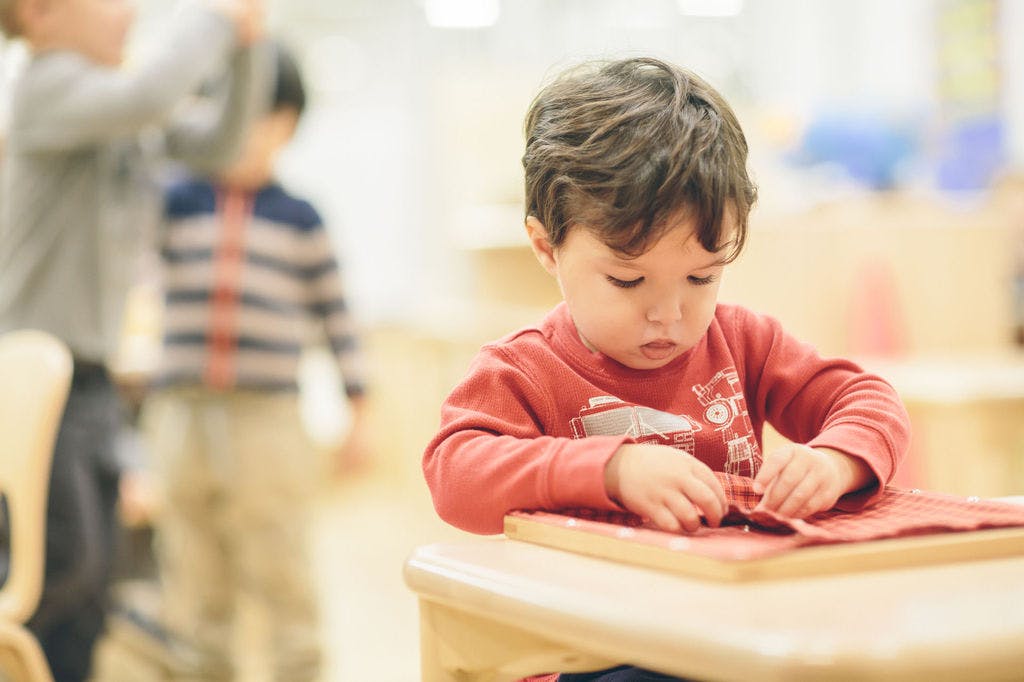 Child in red shirt working with fabric on a table in a classroom