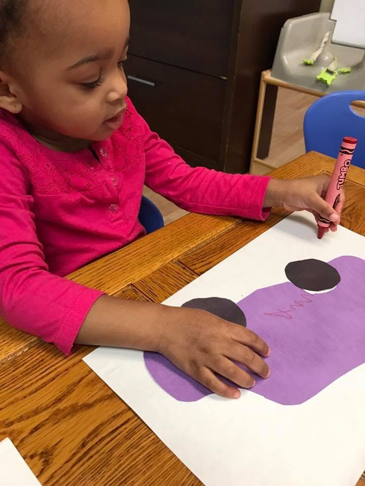 Child drawing on paper with a red crayon