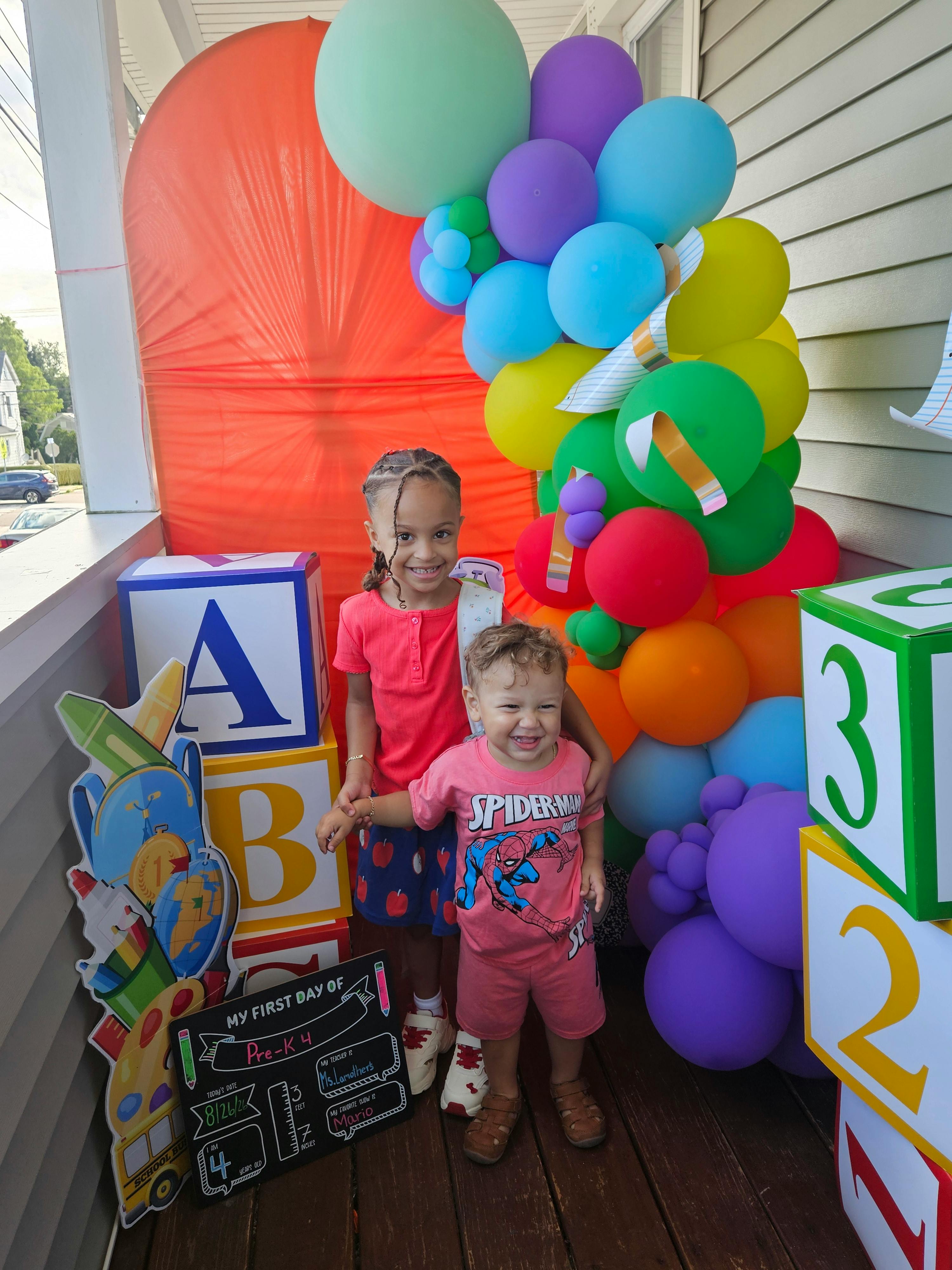 Two children standing in front of school-themed balloons and large letter blocks