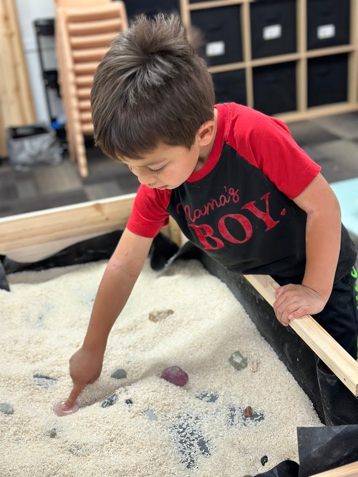 Child playing in a sand table with rice and small rocks