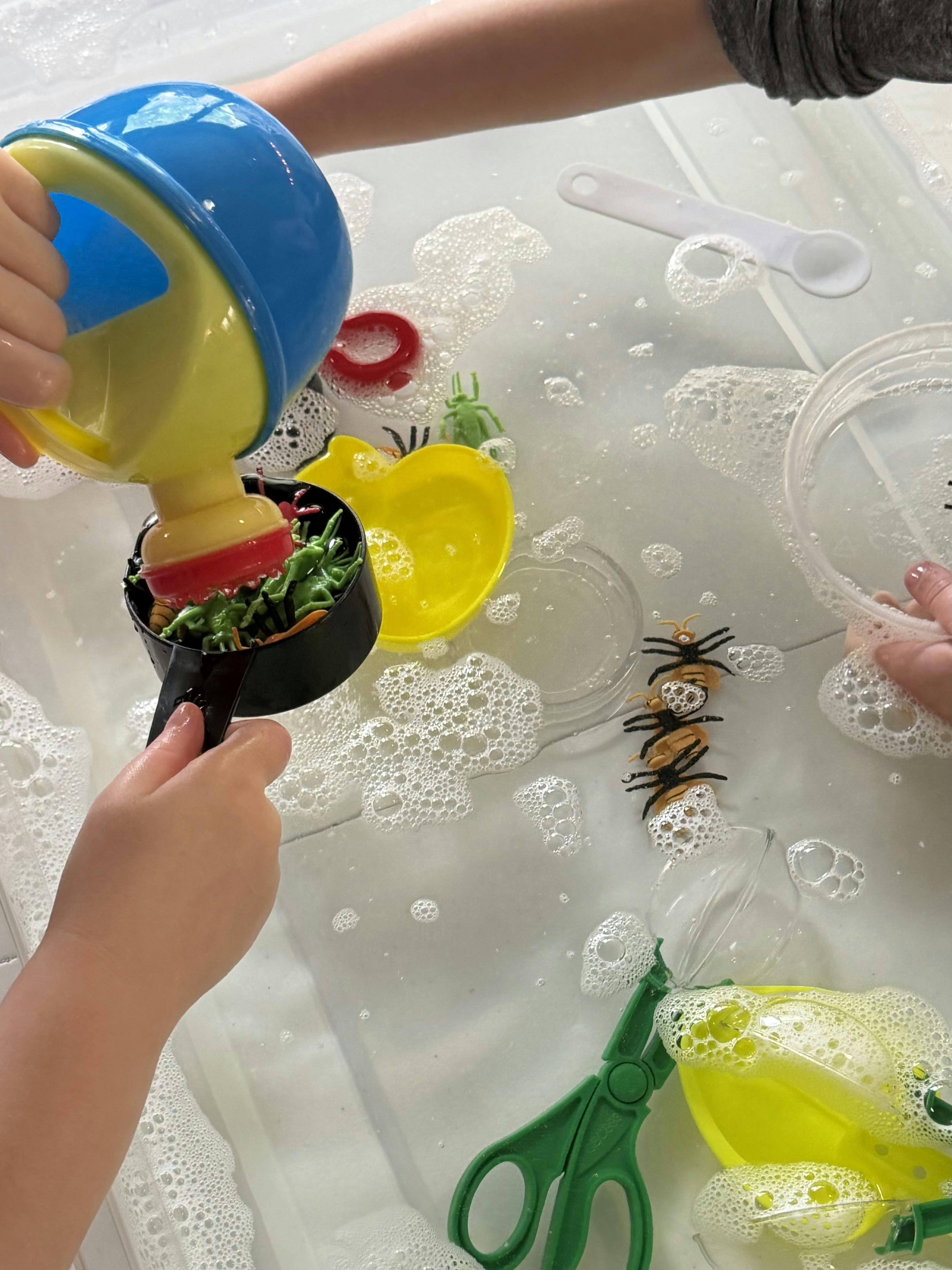 Child playing with plastic insects and scoops in a bin of soapy water