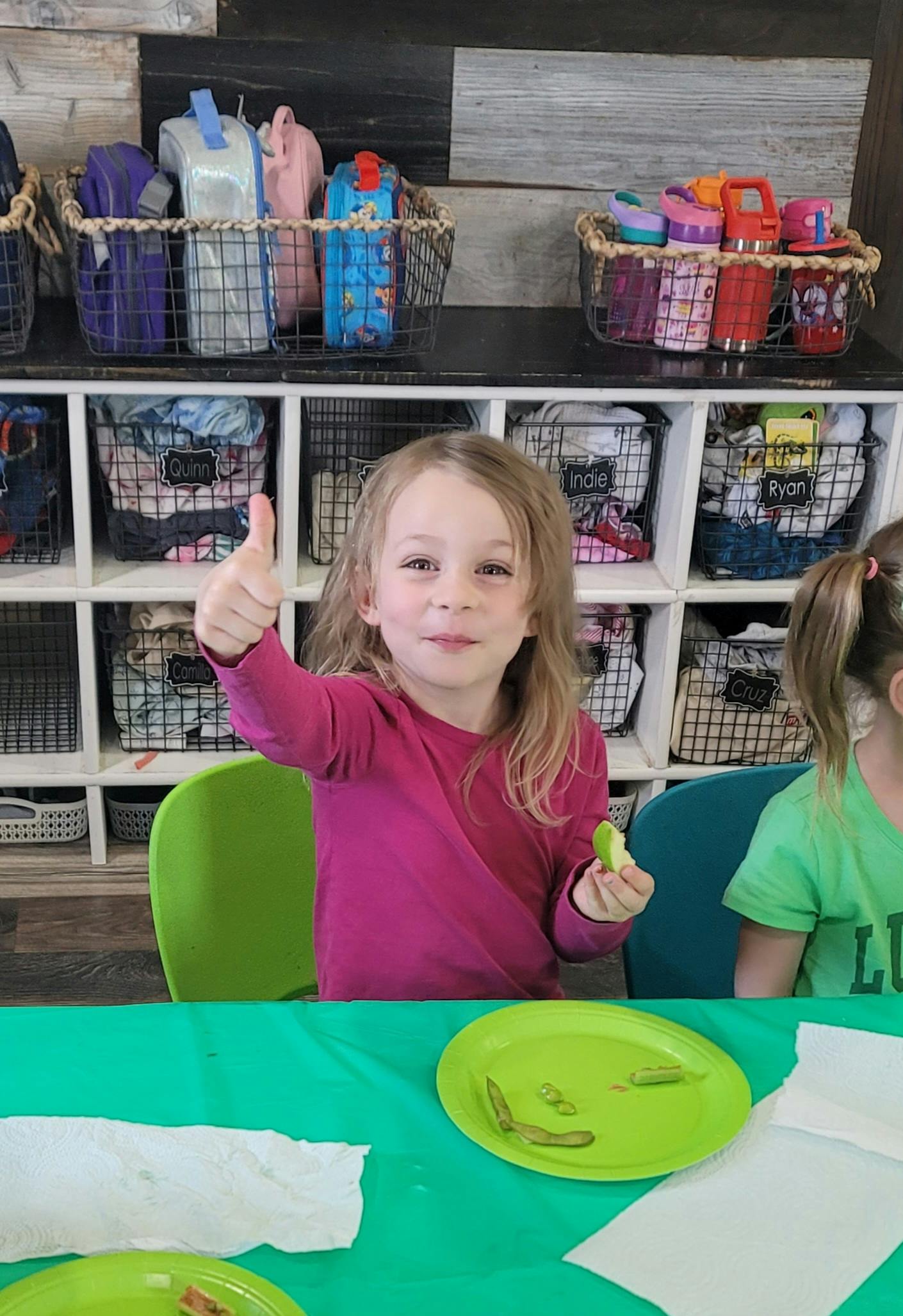 Child giving a thumbs up while holding food at a table