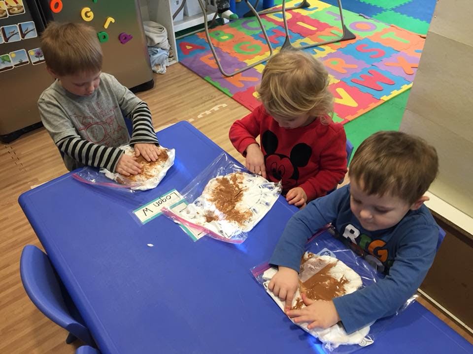 Three children mixing ingredients in plastic bags at a blue table