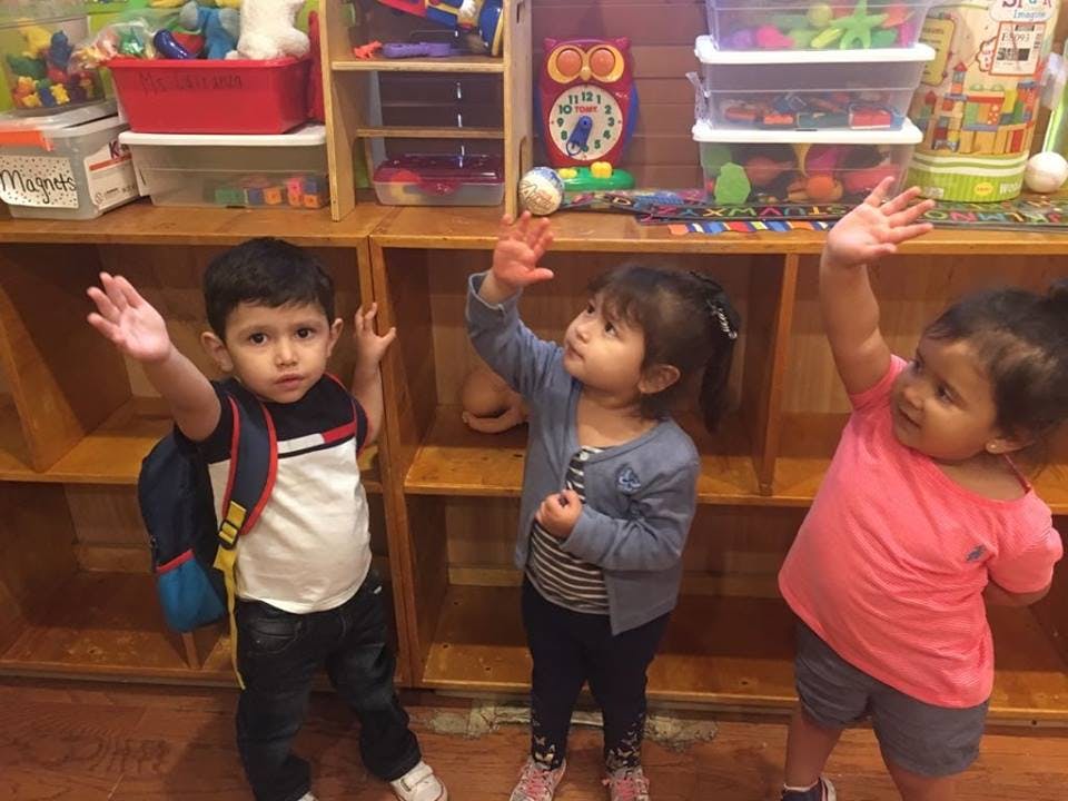 Three children with arms raised in a classroom